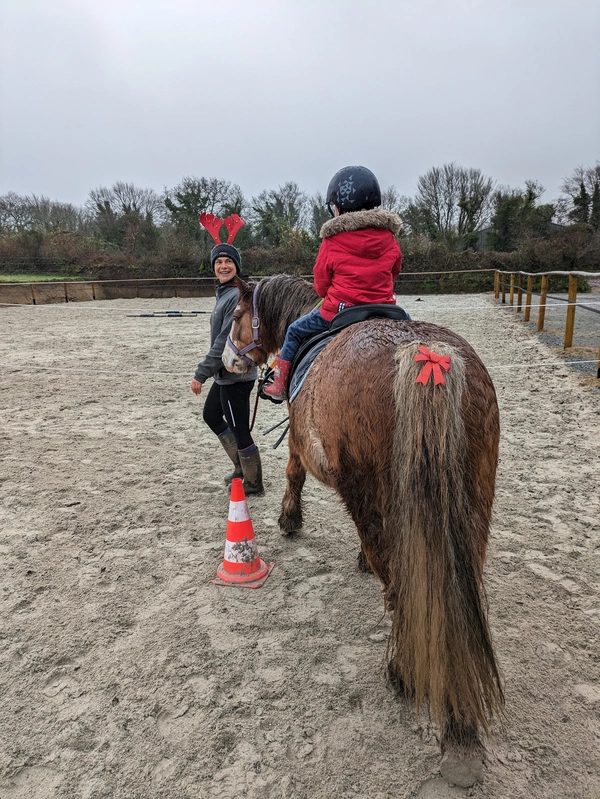 Un cours d'équitation,: la monitrice tient le poney de l'enfant.